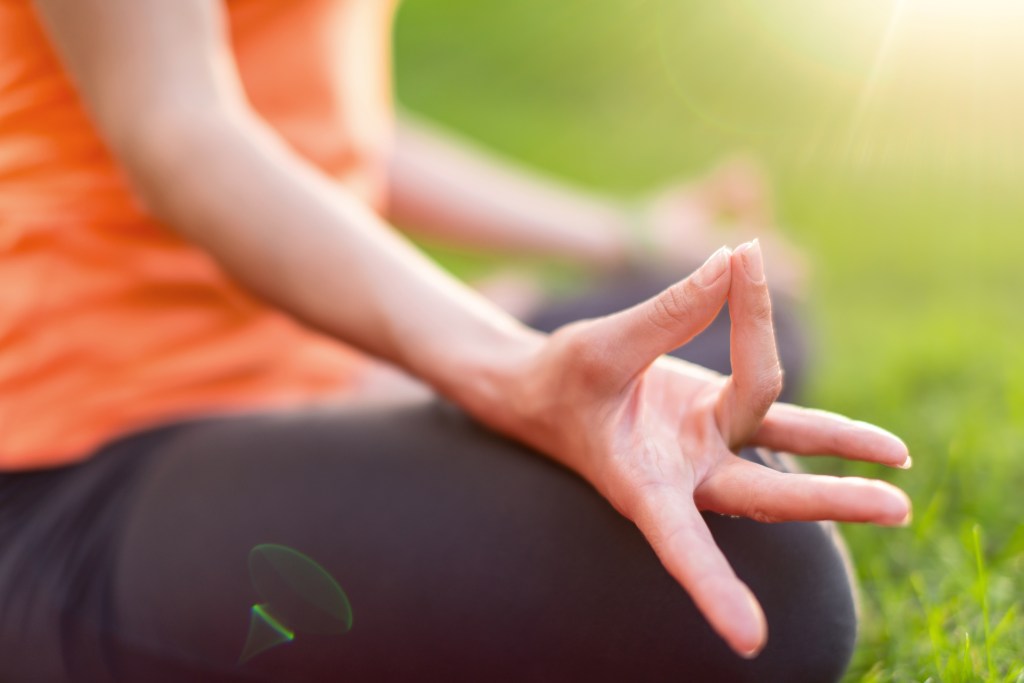 Hand detail of a girl meditation and taking a yoga pose at sunset under trees